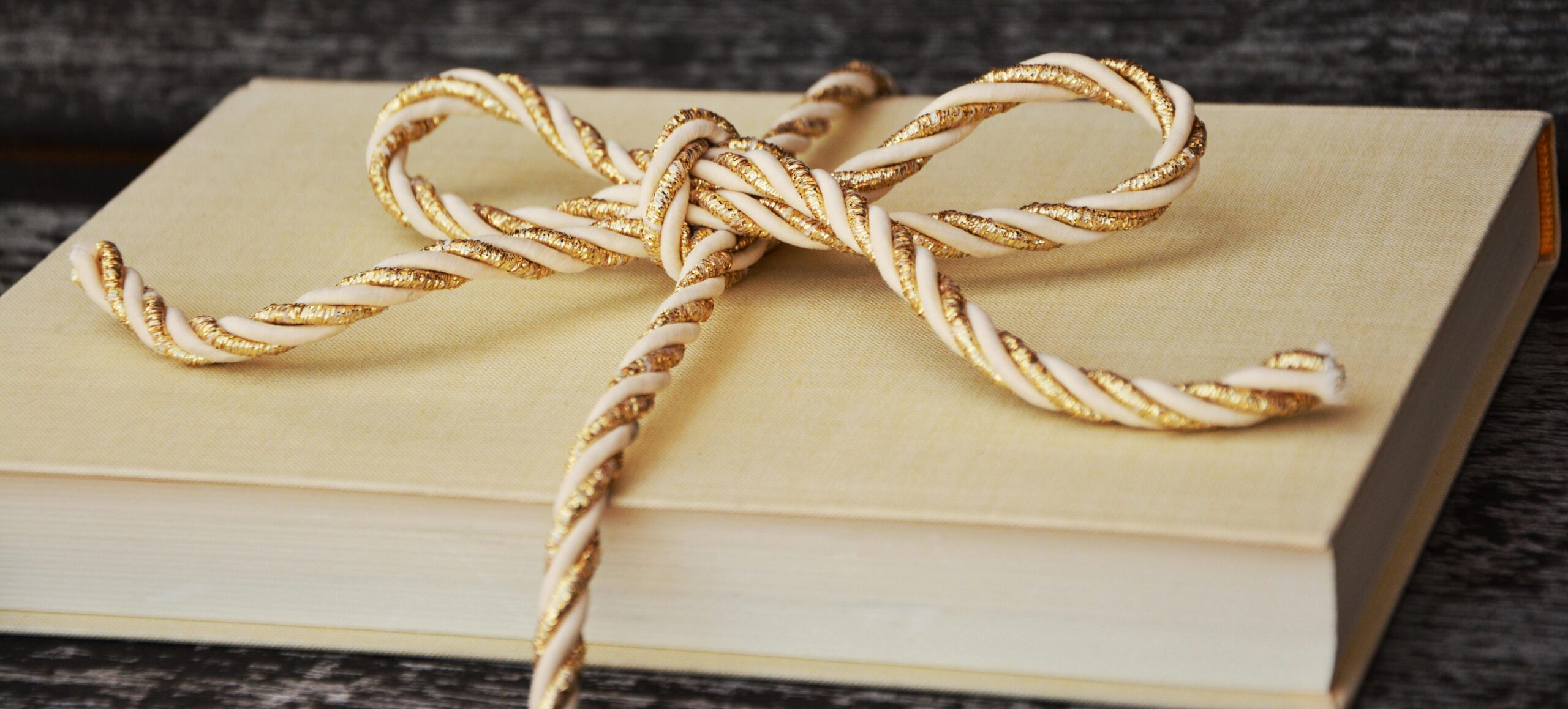 Picture of a pale yellow book wrapped in a good and white rope tied into a bow